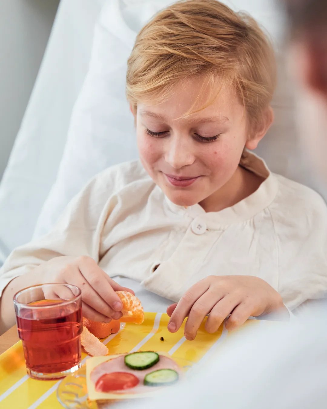 A little boy sitting in a hospital bed with a tray of food.